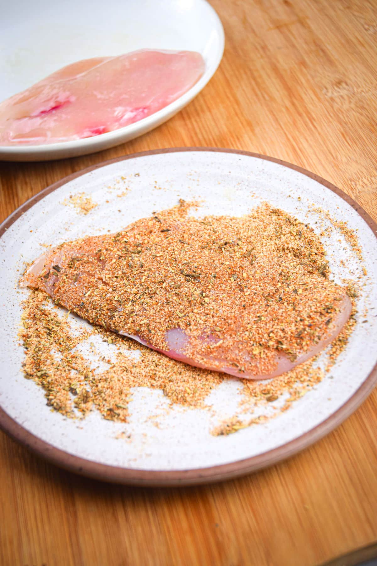 Raw chicken breast covered in blackening spices on plate.