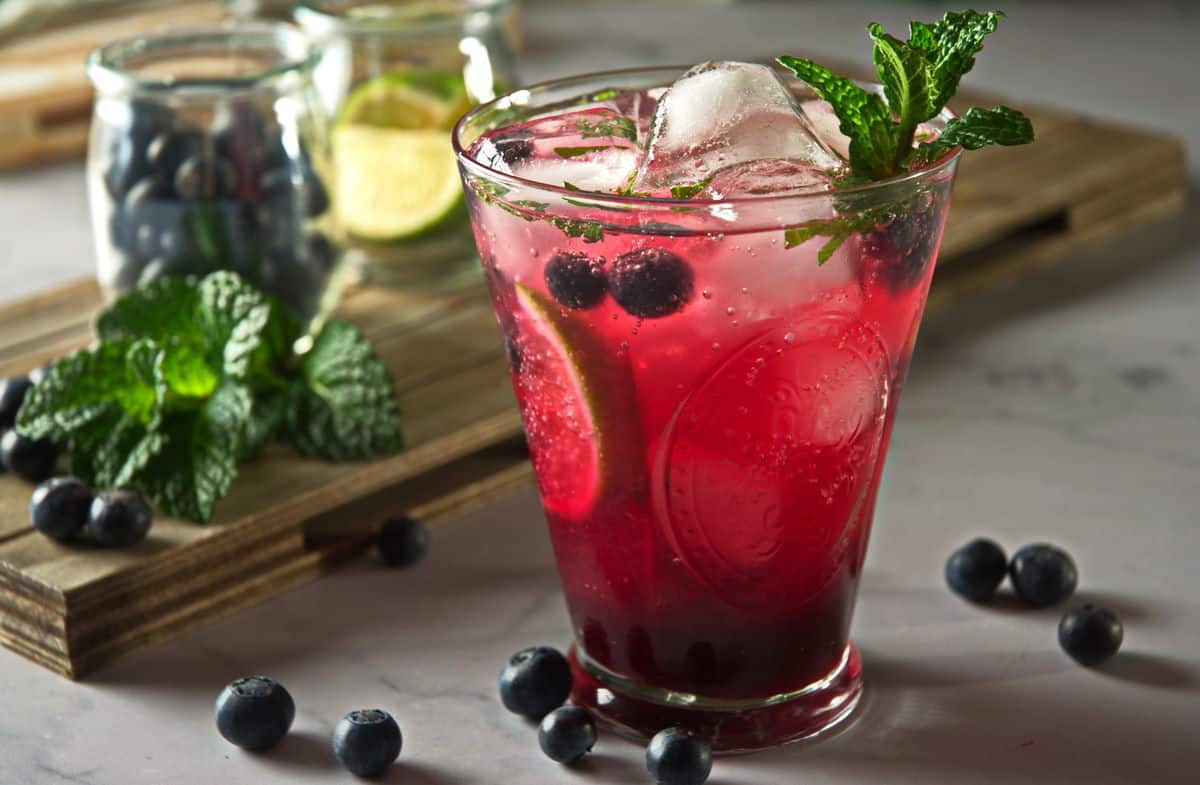 Blueberry mojito mocktail in a glass with fresh blueberries scattered around the glass.