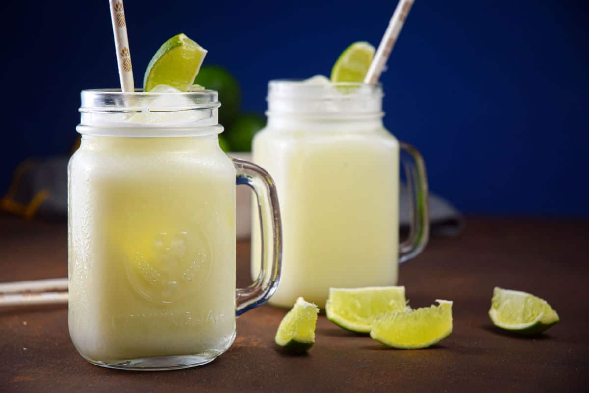 Brazilian Lemonade Suica-9 Brazilian lemonade in glass jars with lime wedges and paper straws.