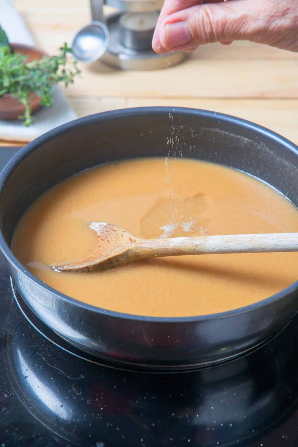 Brown gravy in frying pan with a wooden spoon and salt sprinkling on top.