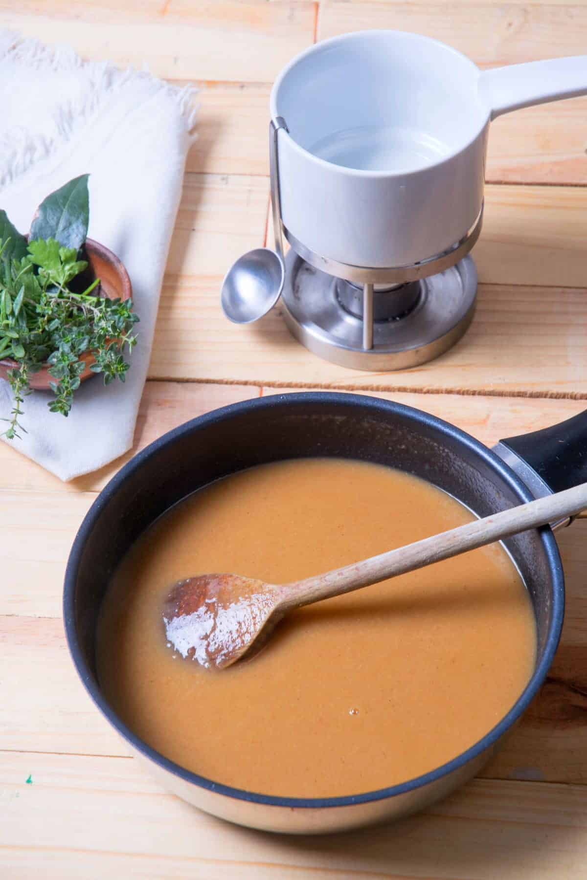 Brown gravy in frying pan on wooden background, gravy warmer in the background.