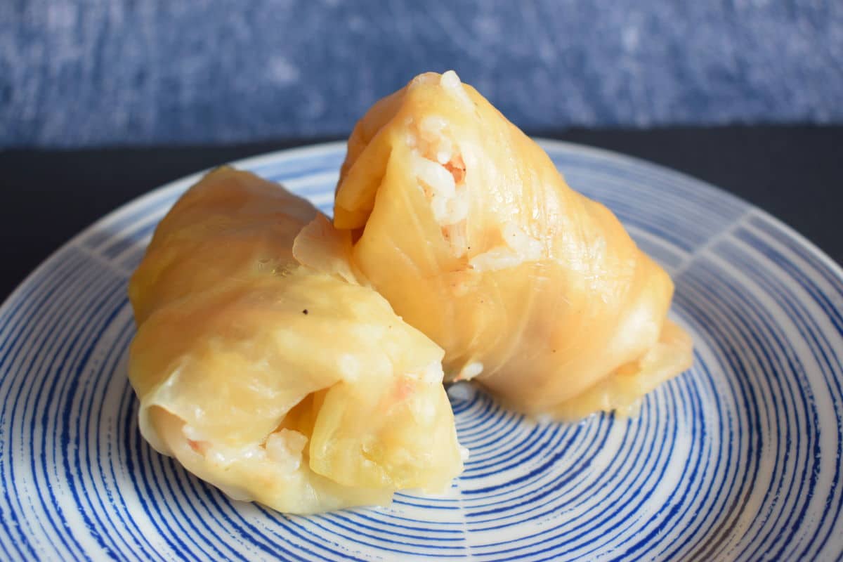 Cooked cabbage rolls stacked on blue plate.