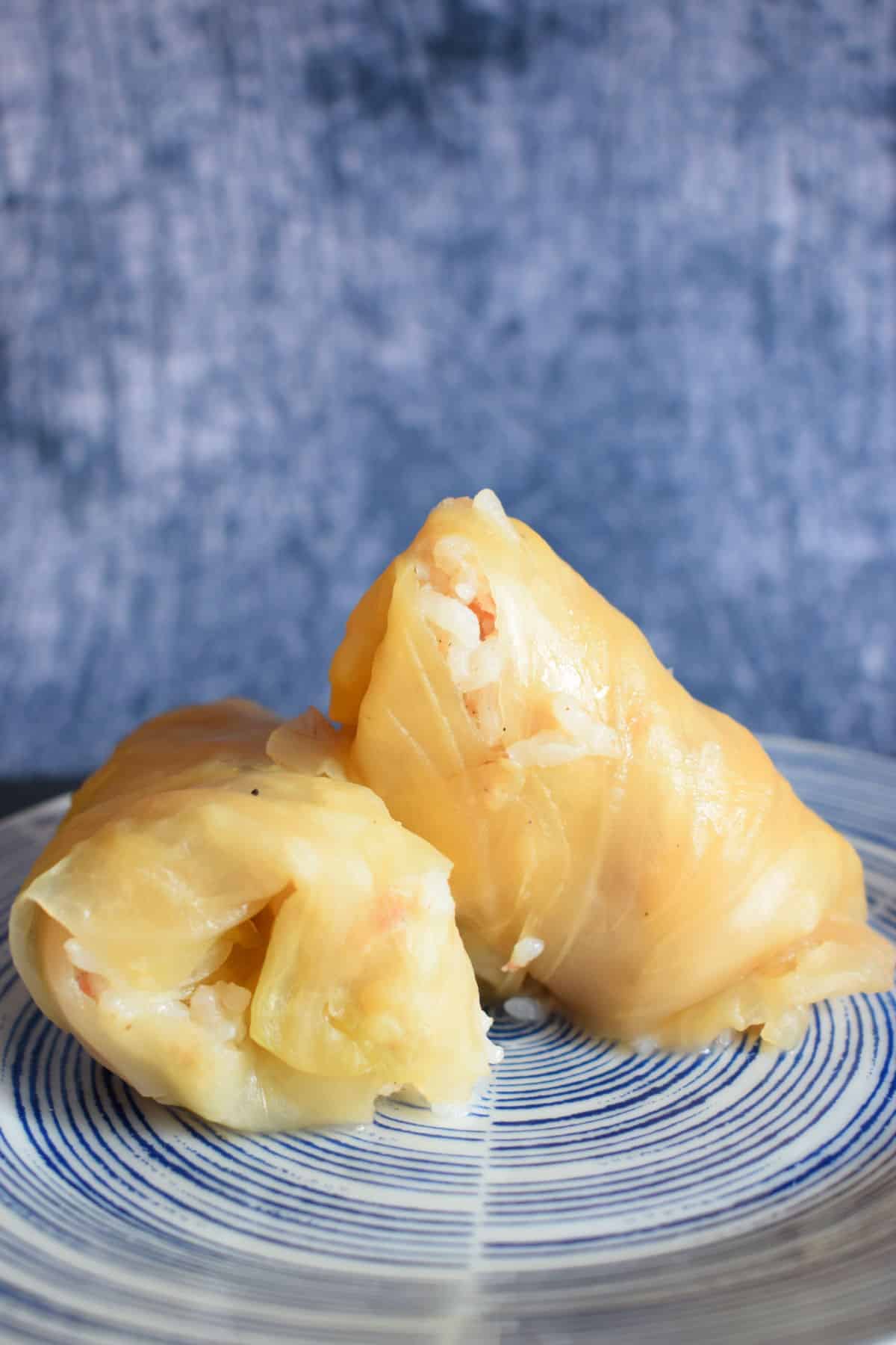 Cooked cabbage rolls stacked on blue plate.