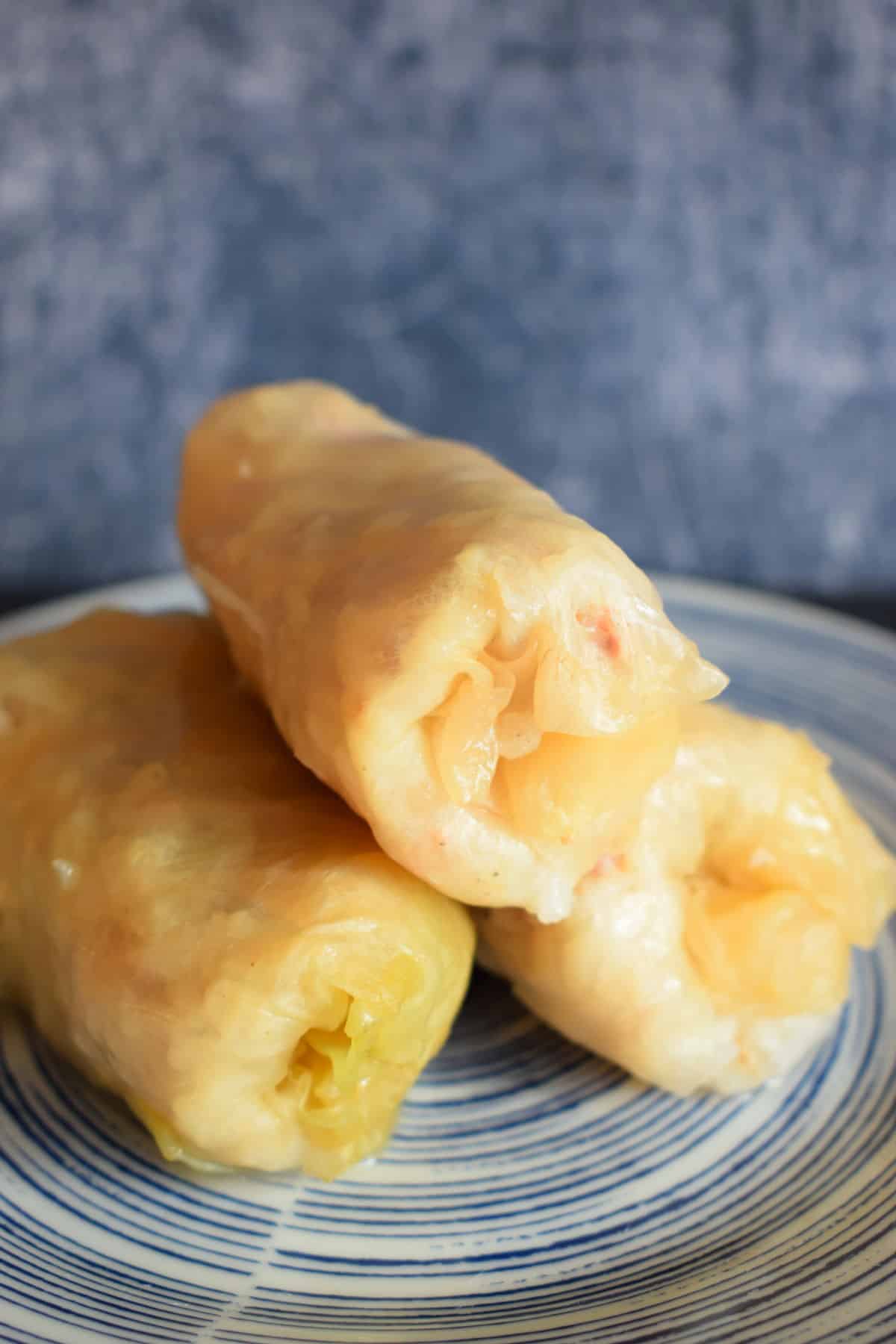 Cooked cabbage rolls stacked on blue plate.