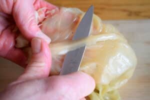 Hand cutting cabbage leaf with paring knife.