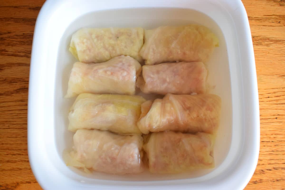 Unbaked cabbage rolls in casserole dish with boiling water.
