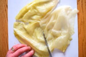Cabbage leaf cut into 3 pieces on cutting board.