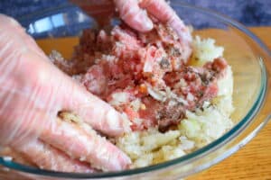 Hands mixing cabbage roll stuffing in bowl.