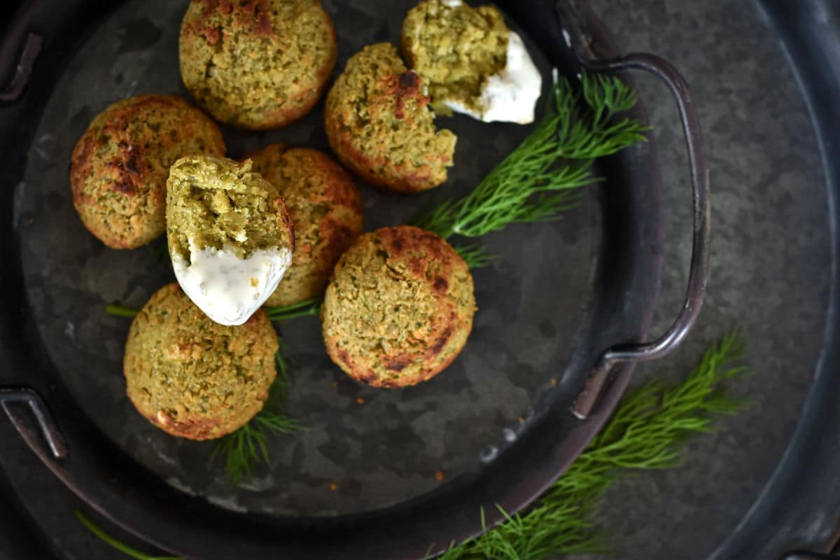 Mini falafel bites with fresh dill and yogurt on black plate.