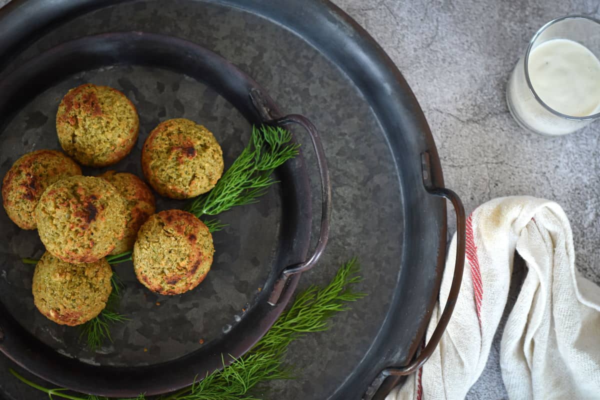 Mini falafel with fresh dill on black plate.