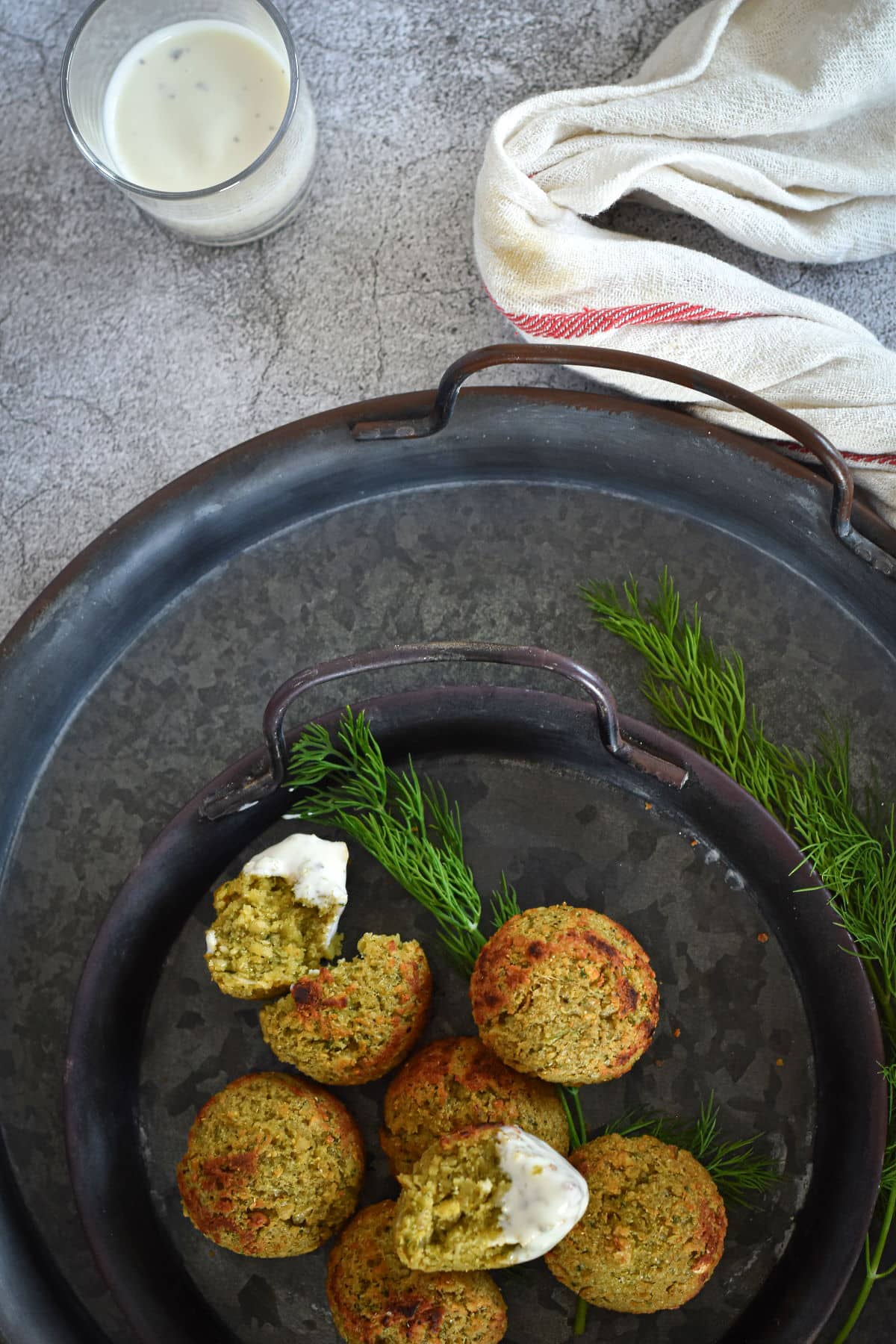 Mini falafel bites with yogurt sauce on black plate.