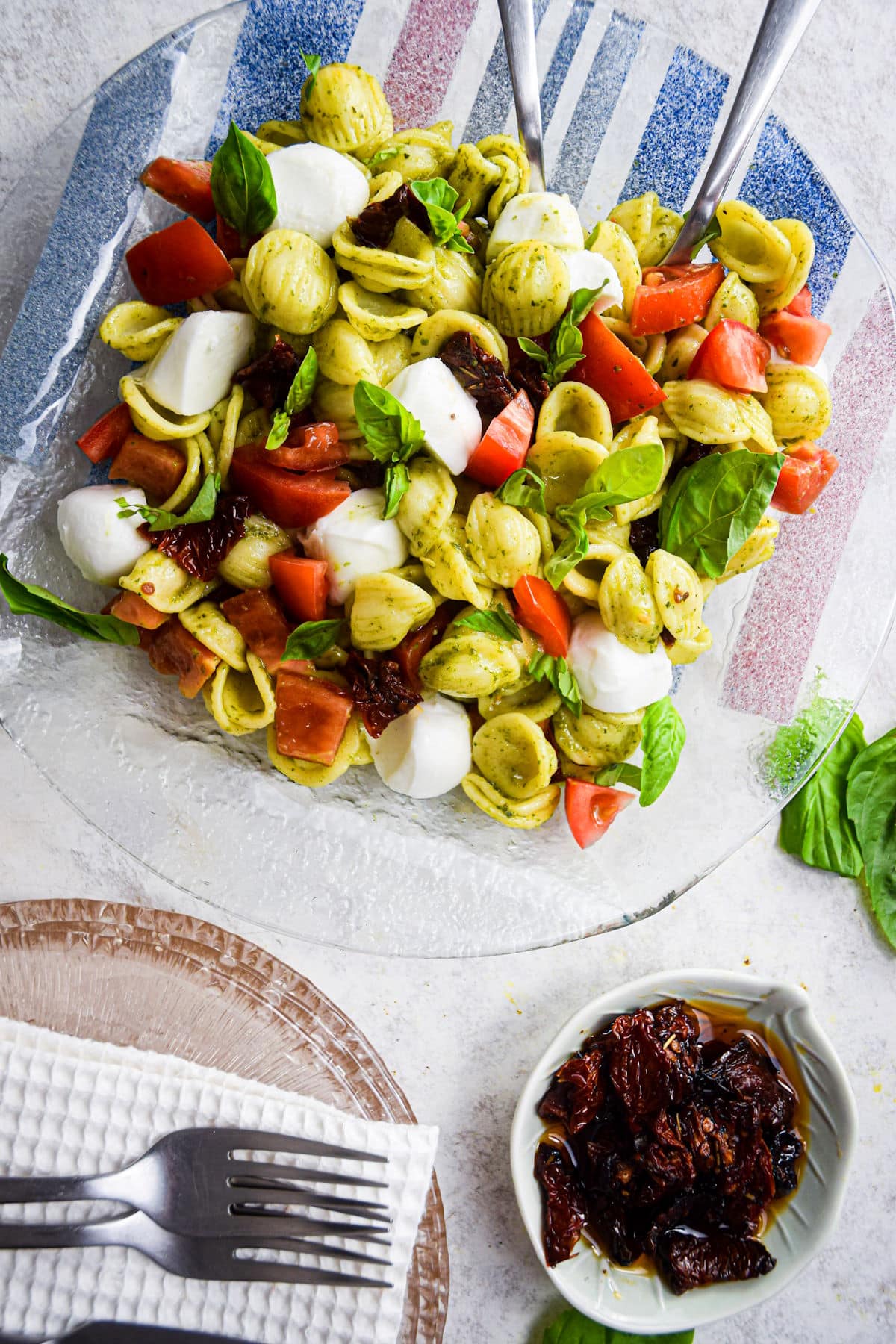 Caprese pasta salad with tomatoes and mozzarella on clear glass plate.