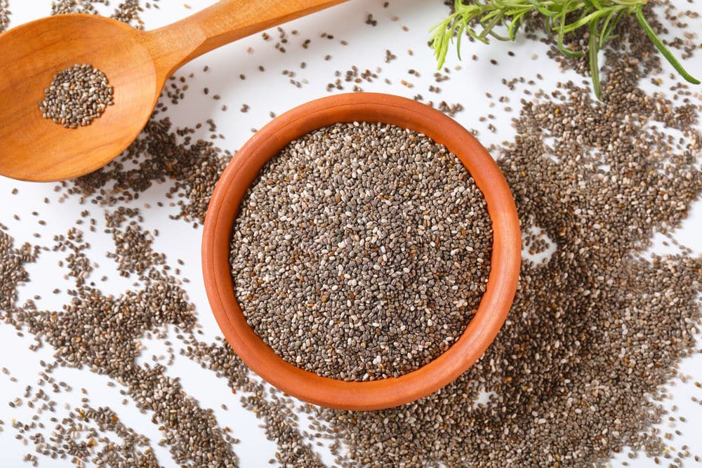 bowl of healthy chia seeds and wooden spoon on white background