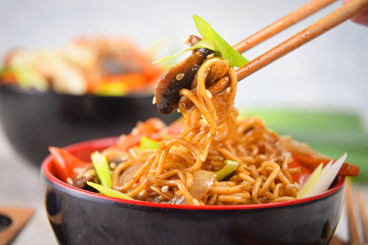 Chicken lo mein noodles in black and red bowl with chop sticks.