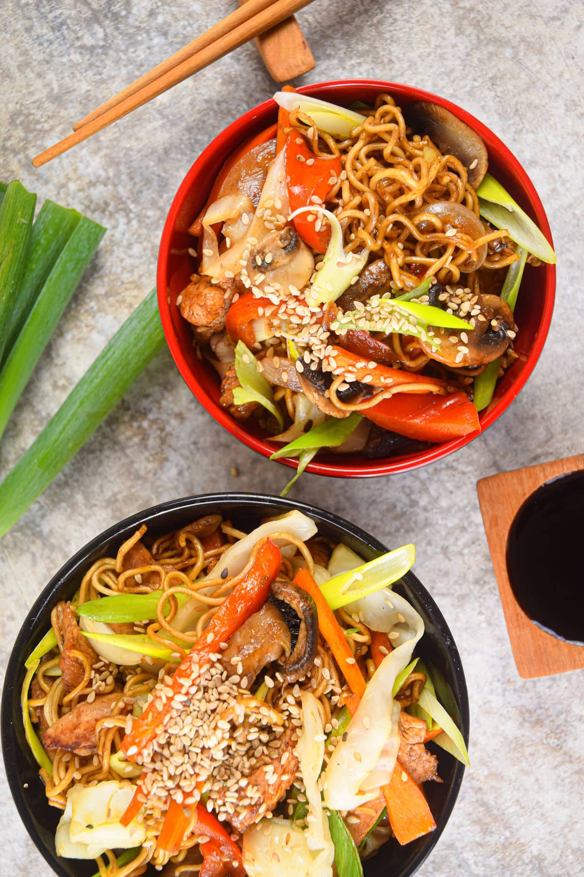 Chicken lo mein noodles in red and black bowls with chop sticks and sauce on the side.