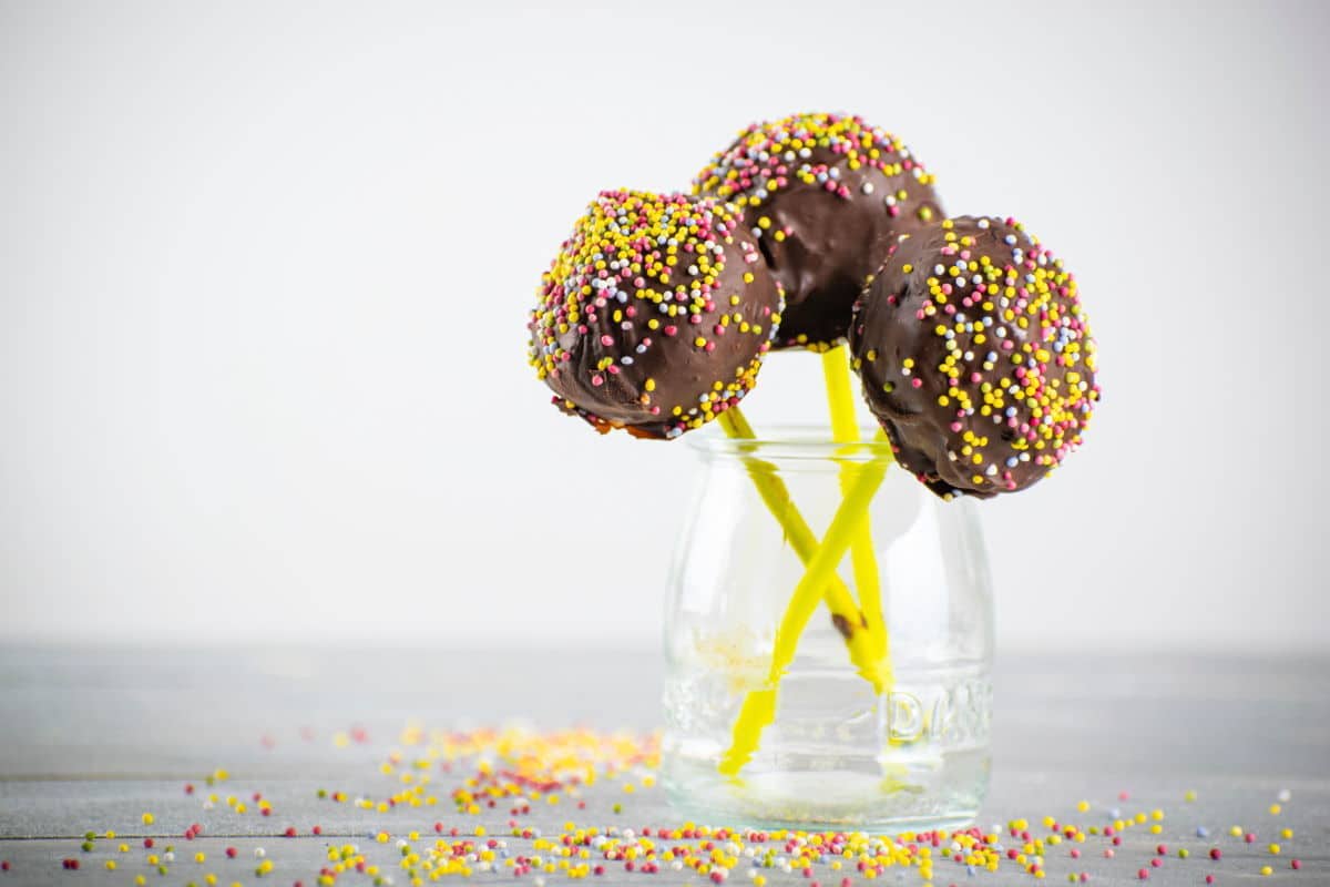 How to Make Cake Pops With a Mold 2-3 Chocolate covered cake pops with sprinkles in glass jar.