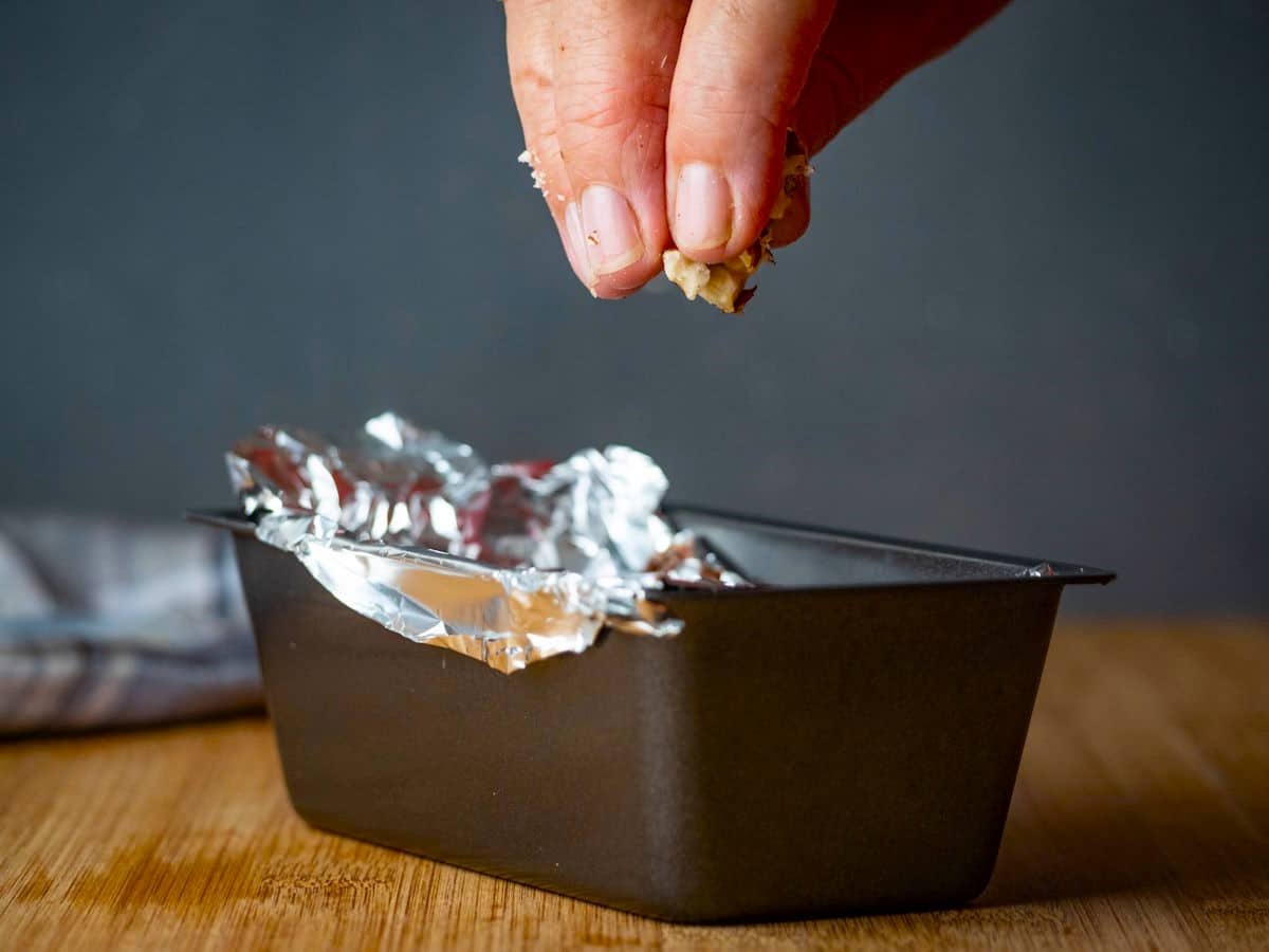 Hand holding hazelnuts over loaf pan.