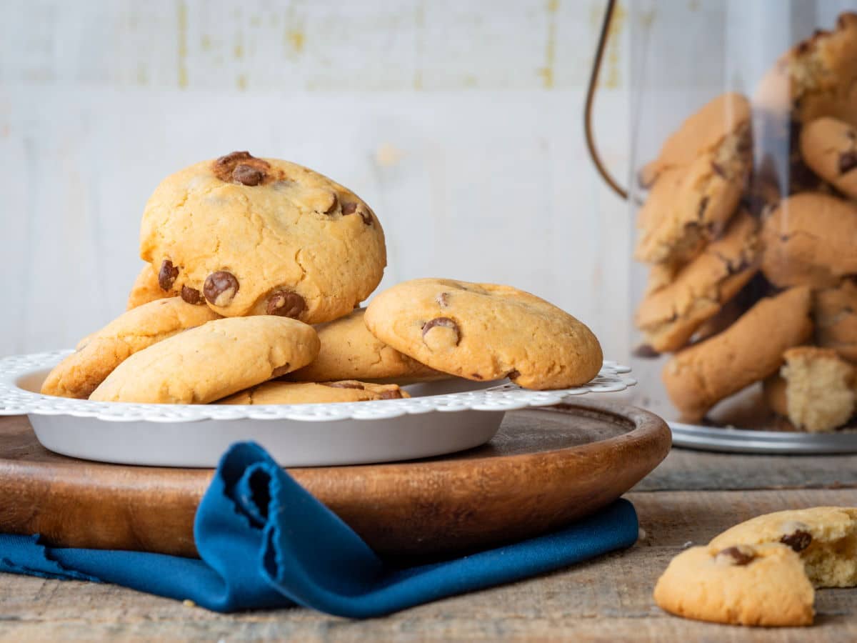 Chocolate chunk cookies on a white plate with a cookie jar in the background.
