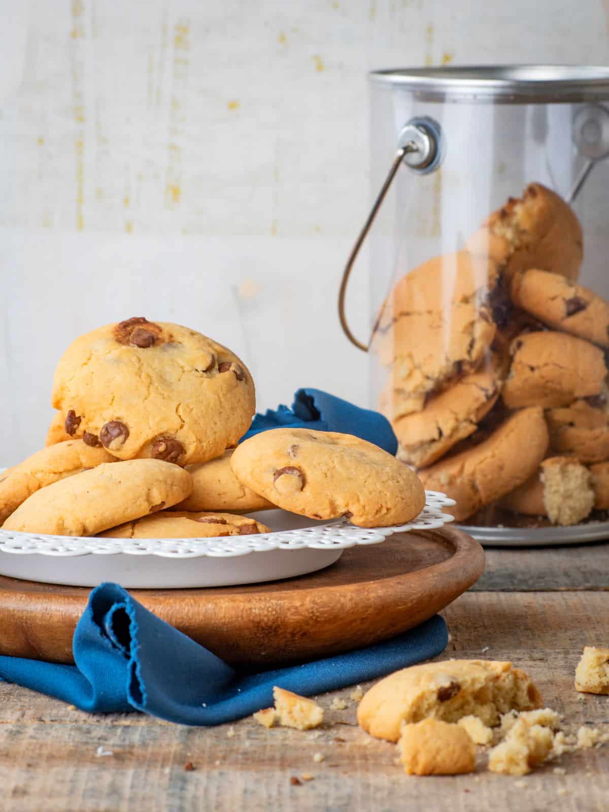 Chocolate chunk cookies on a white plate with a cookie jar in the background.