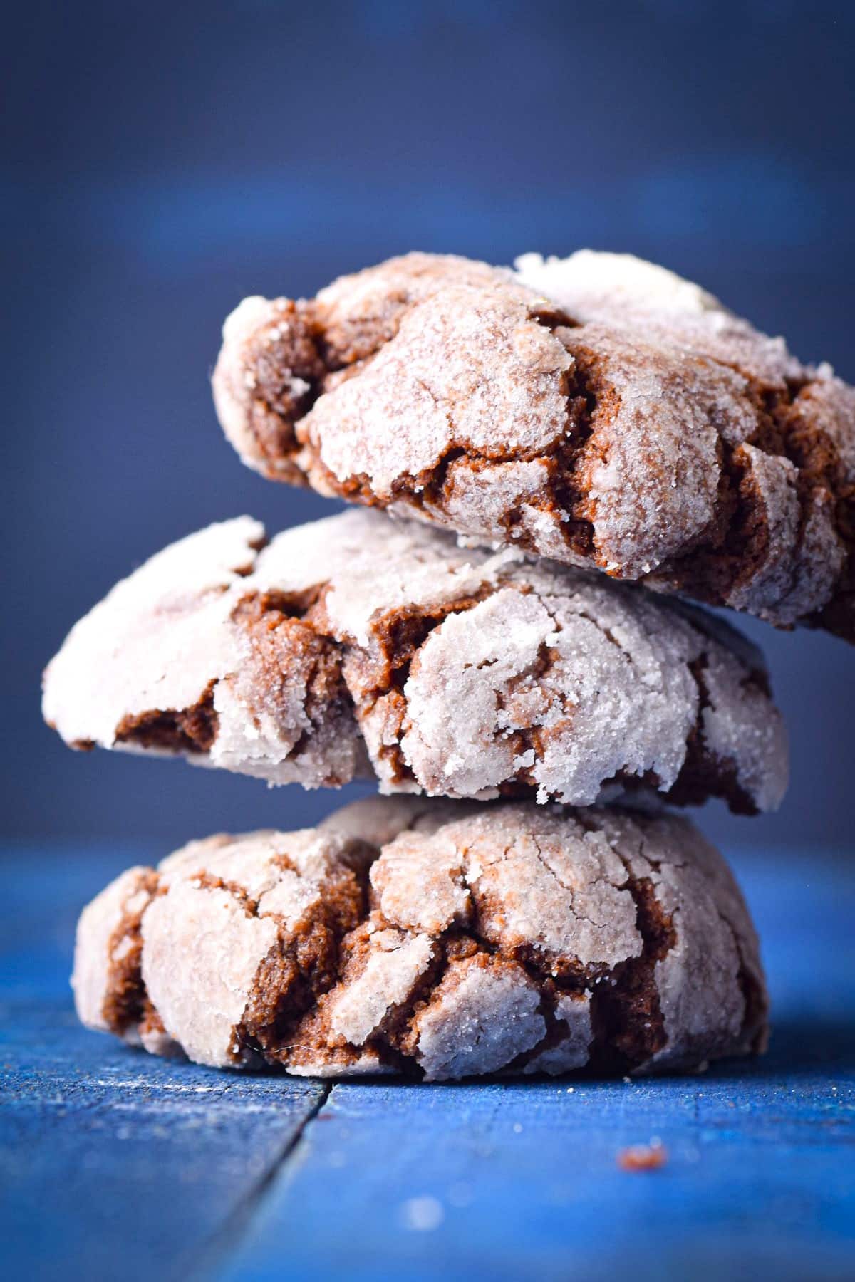 Chocolate crinkle cookies stacked on blue background.