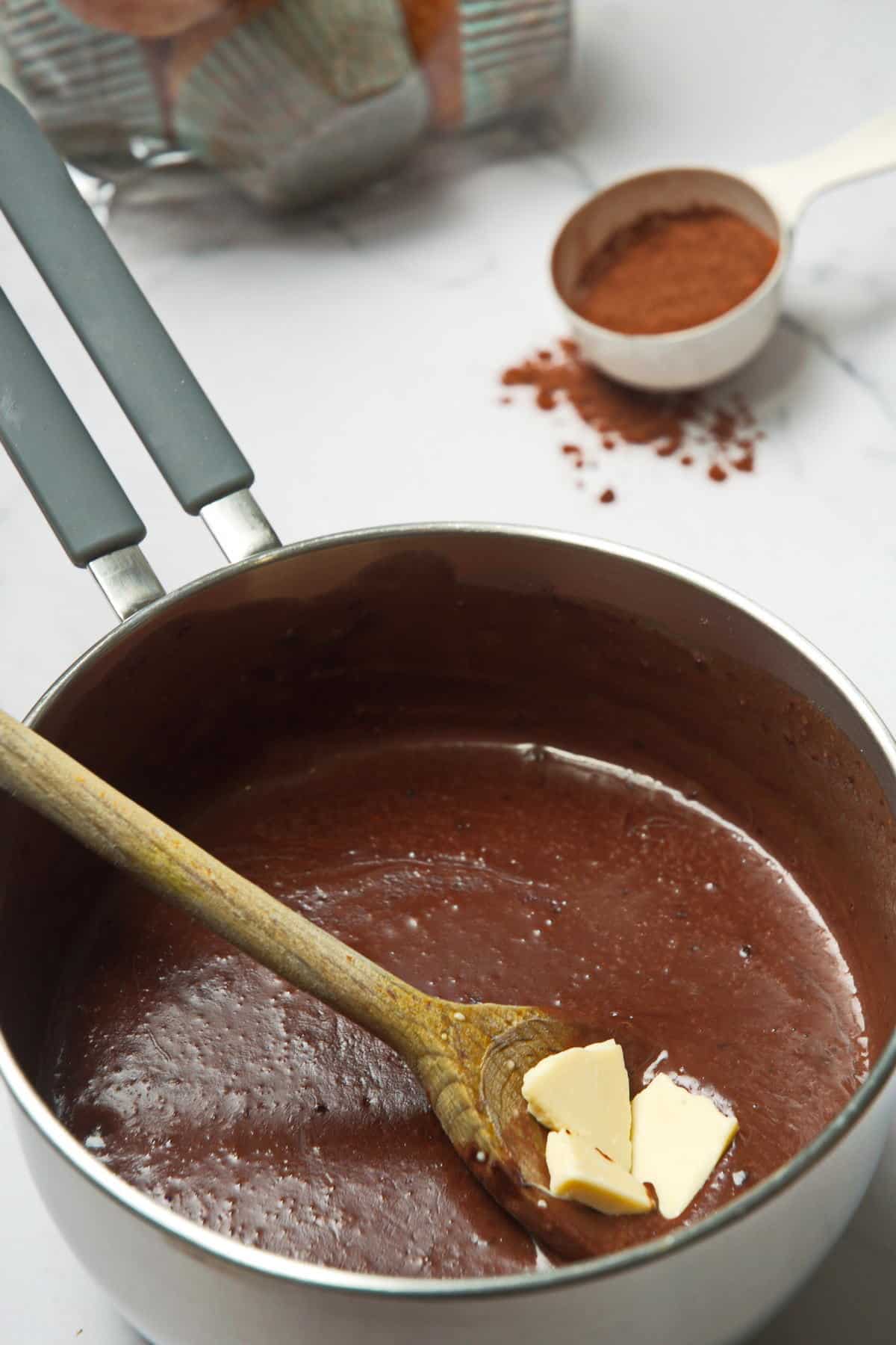 Chocolate gravy in a saucepan with wooden spoon and white chocolate pieces.