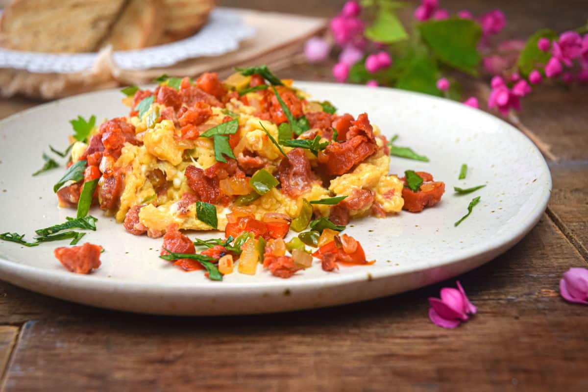 Chorizo and scrambled eggs on a white plate with parsley.