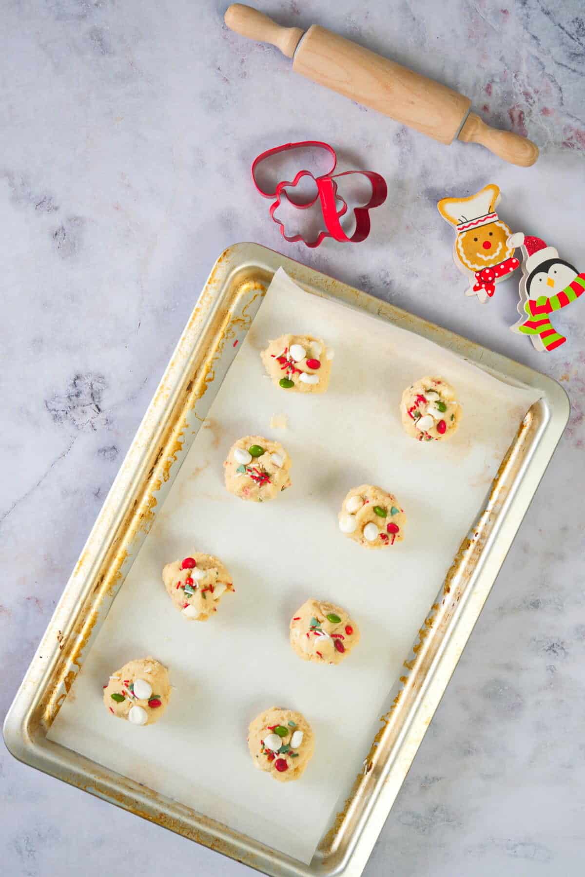 Christmas cookie dough balls on a parchment lined baking sheet, with Christmas cookie cutters and rolling pin on the side.