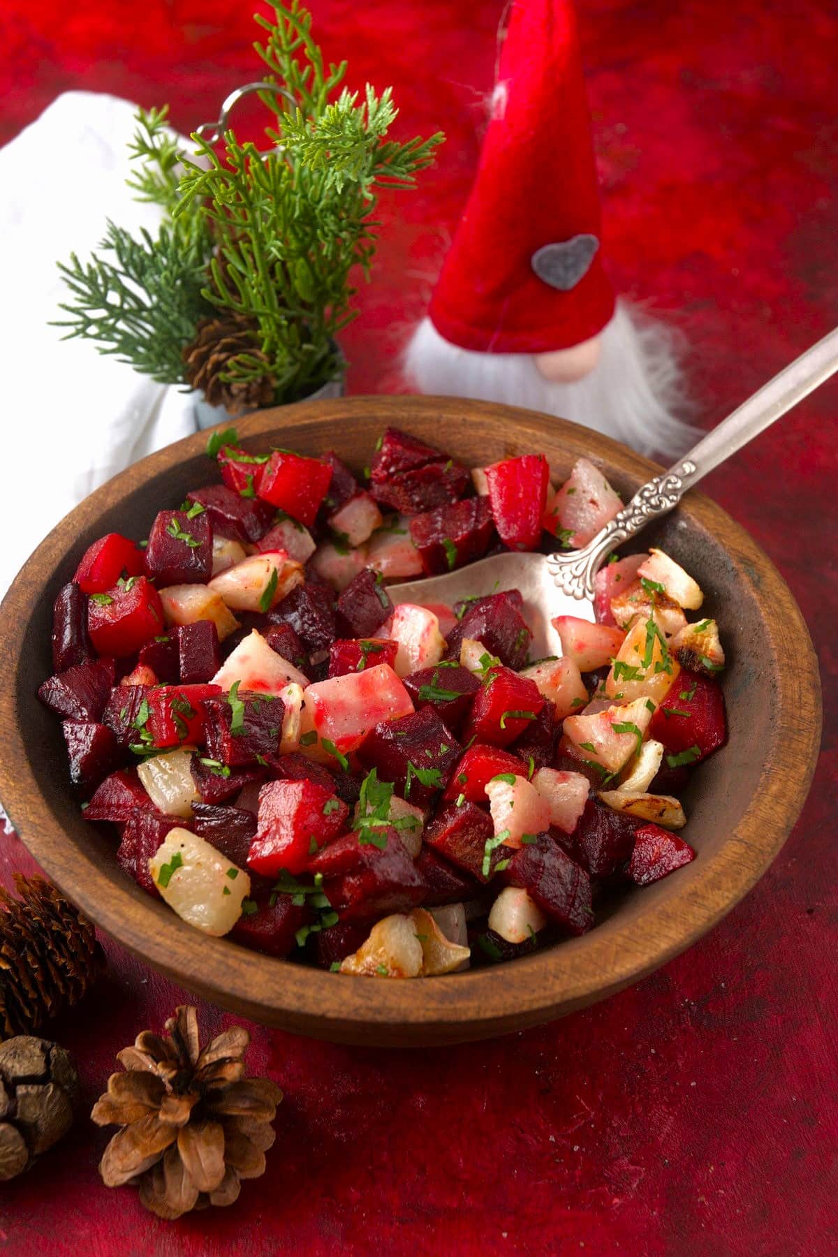Roasted beets and turnips in wooden serving bowl with Christmas decorations and serving spoon.
