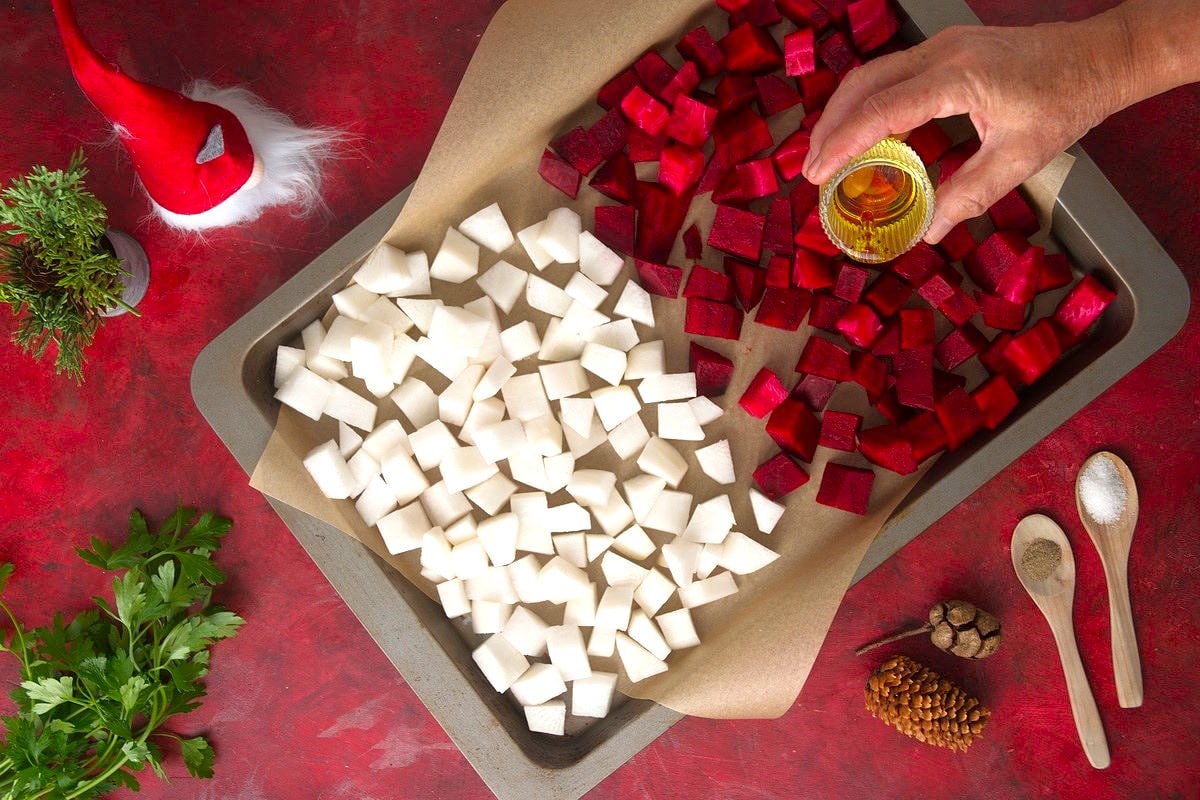 Chopped beets and turnips on a baking sheet with Christmas decorations on the side.