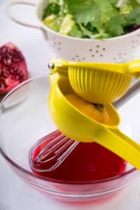 Pomegranate dressing in a small bowl with a whisk and lemon juicer over top.