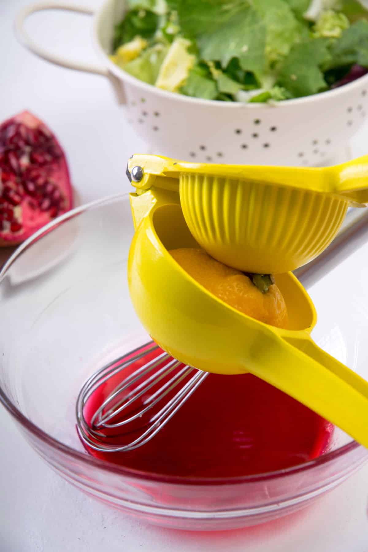 Pomegranate dressing in a small bowl with a whisk and lemon juicer over top.