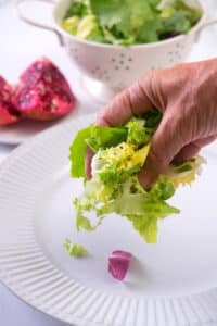 Greens getting placed on a white serving plate.