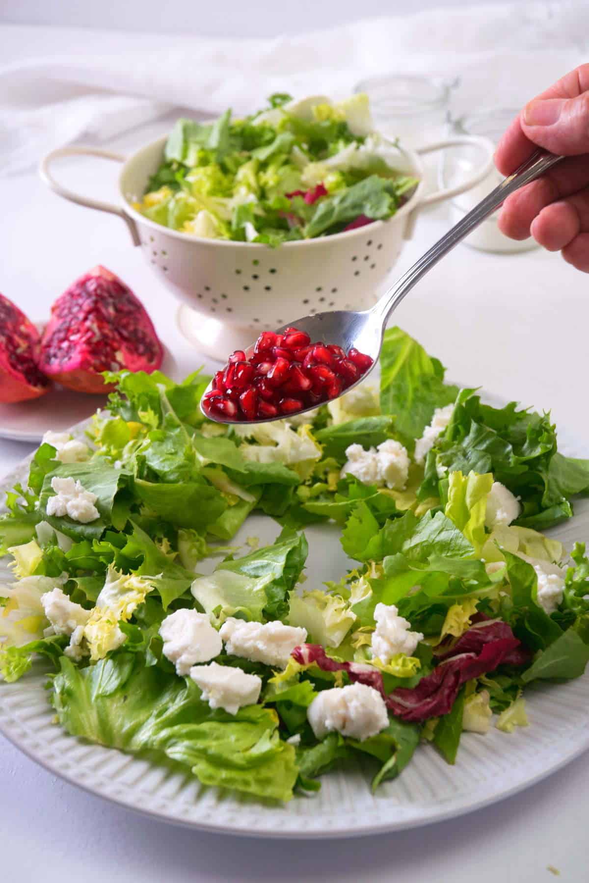 Greens on a serving plate in the shape of a wreath with pomegranate seeds and goat cheese.