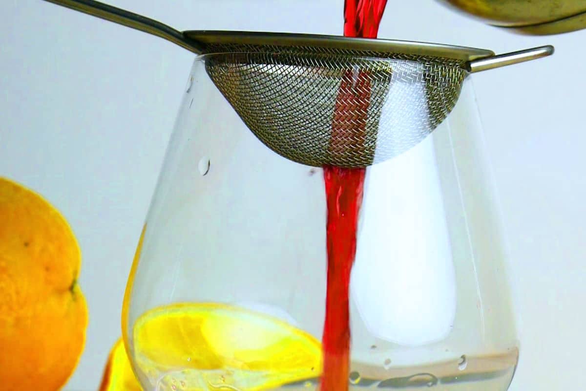 Swedish Glögg straining into wine glass through wire mesh strainer.
