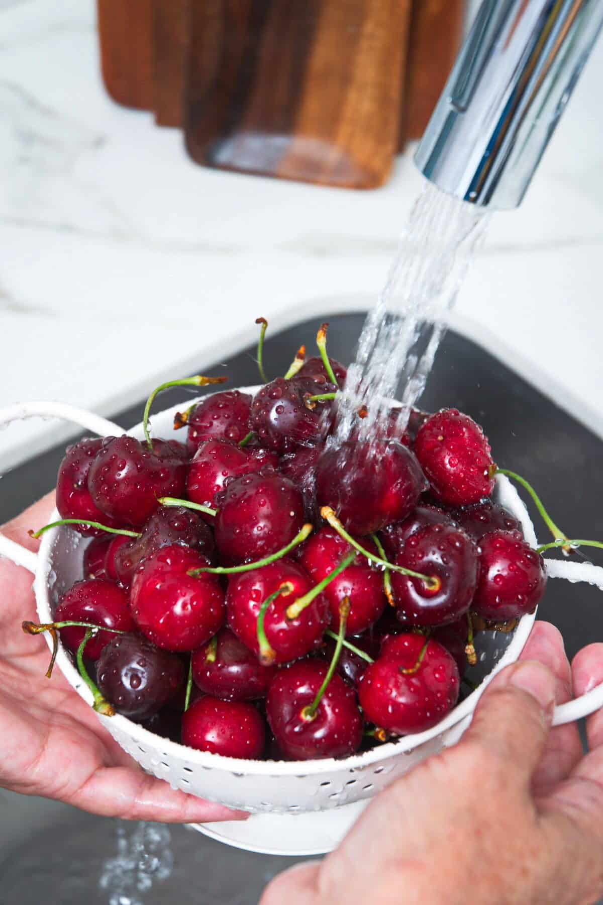 Cherries in a colander with water running over them.