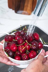 Cherries in a colander with water running over them.