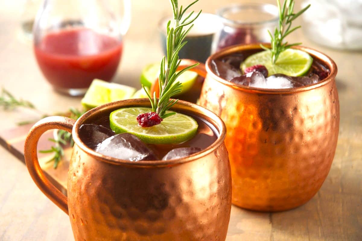 Cranberry Moscow mule in copper mugs with cranberry, lime and rosemary.
