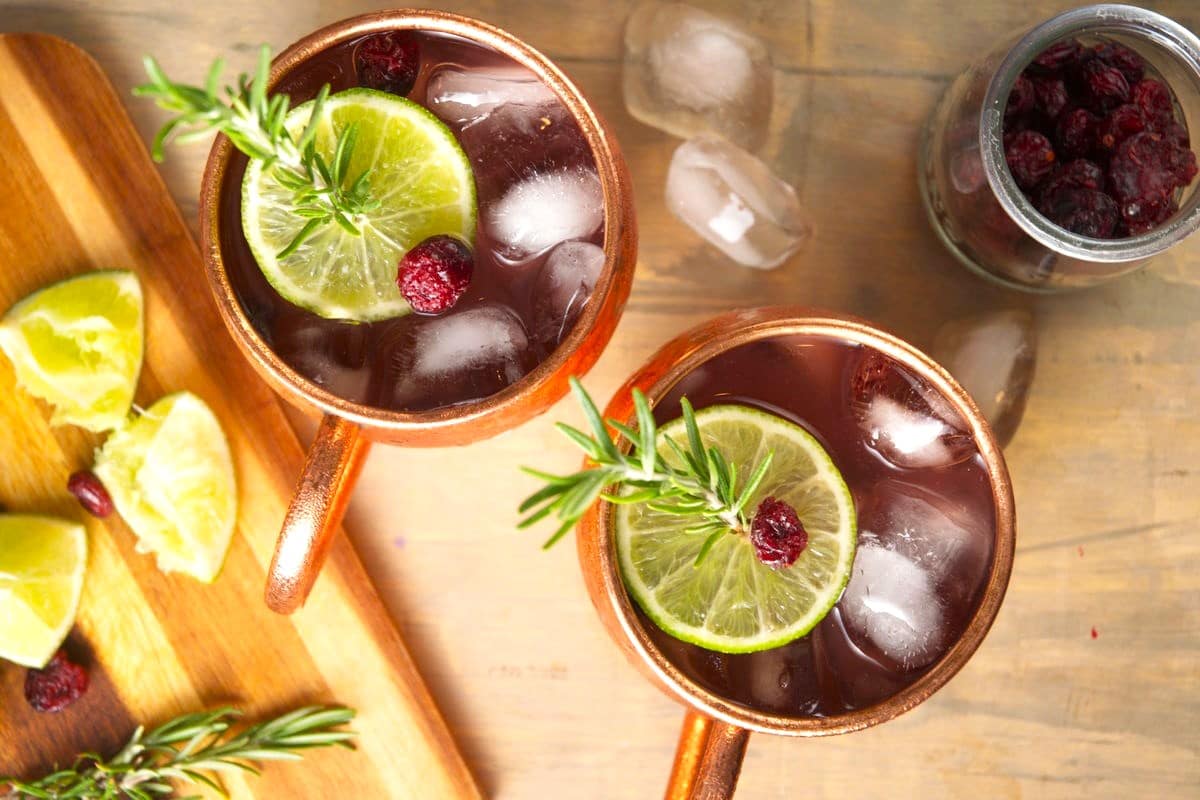 Cranberry Moscow mule in copper mugs with cranberries, lime slices and rosemary.