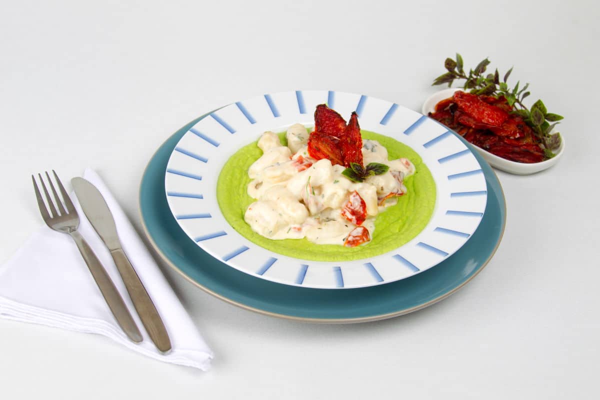 Gnocchi and pea puree with sundried tomatoes in dish. A fork and knife on the side.