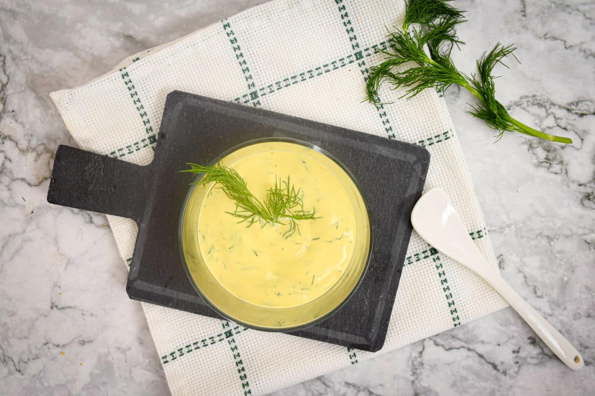Dill dip in a glass serving dish with fresh dill sprigs and a small white spoon.