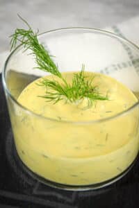Dill dip in a glass serving dish with a fresh dill sprig.