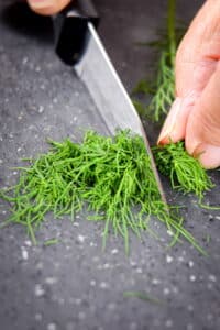Dill being chopped with a knife on cutting board.
