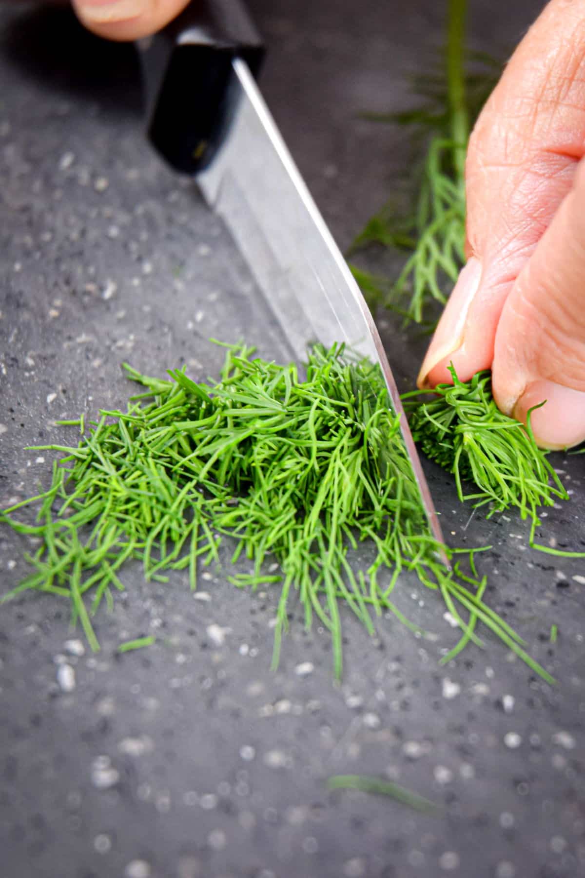 Dill being chopped with a knife on cutting board.