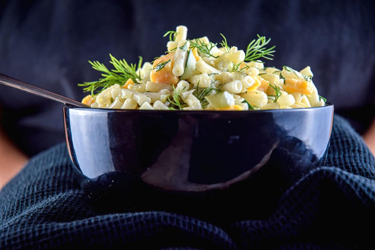 Woman holding a bowl of dill pickle pasta salad.