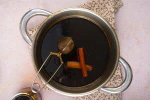 Gingerbread syrup in saucepan with cinnamon sticks and tea infuser.