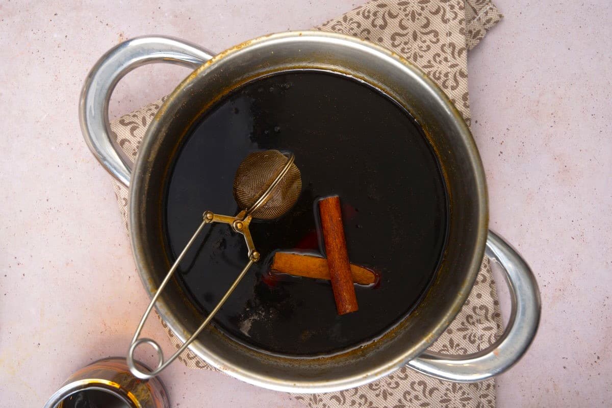 Gingerbread syrup in saucepan with cinnamon sticks and tea infuser.