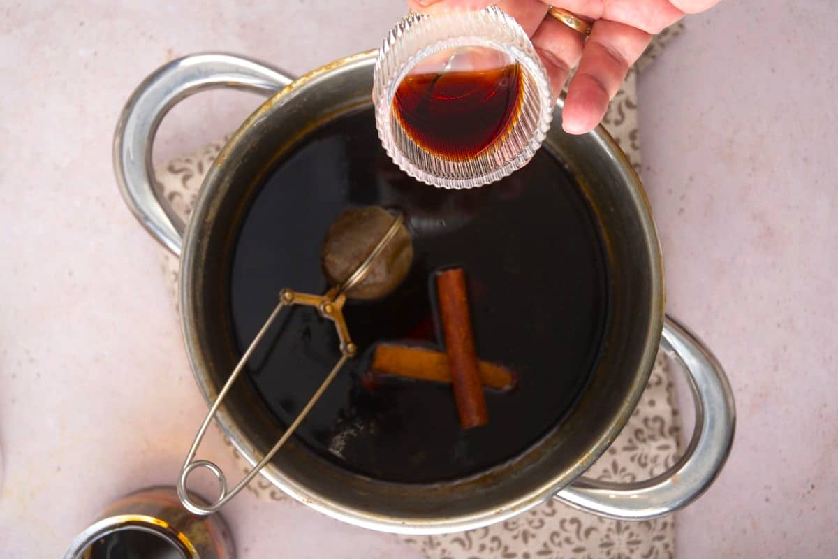 Vanilla extract in small jar over gingerbread syrup in saucepan.