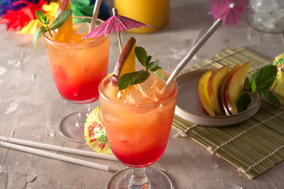 Mai tais in cocktail glasses with umbrellas, mango slices, mint sprigs and straws.
