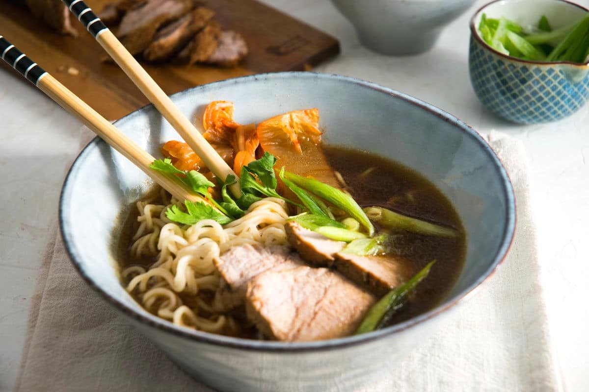 Kimchi ramen with pork slices and chopsticks in a bowl.