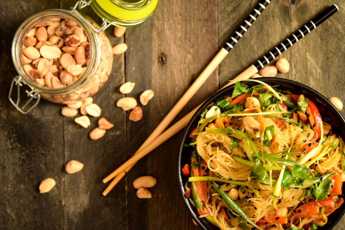 Vegan Pad Thai 4 Vegan Pad Thai in a black bowl with chopsticks and peanuts in a jar on the side.